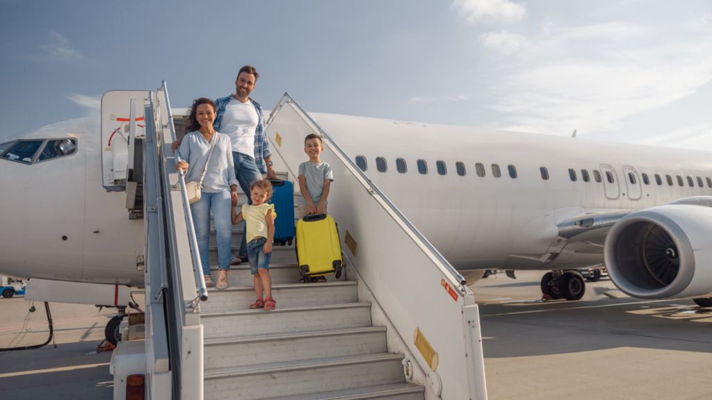 A happy family of four with luggage boarding an airplane via airstairs under a clear sky for a luxury airport transfer.